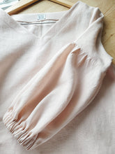 Load image into Gallery viewer, Linen blouse laying flat, showing the gathered sleeve and V-neck line. This natural fabric will keep you warm thru winter and spring. Will also be cool enough to wear thru the summer. Peachy pink shade obtain thru botanical dye of avocado pits. Custom made from medium size to x-large size.
