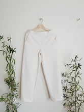 Load image into Gallery viewer, Off white cotton pants, ready to wear for brunch or site seeing.  They are hanging on a light natural wood hanger surrounded by greenery.
