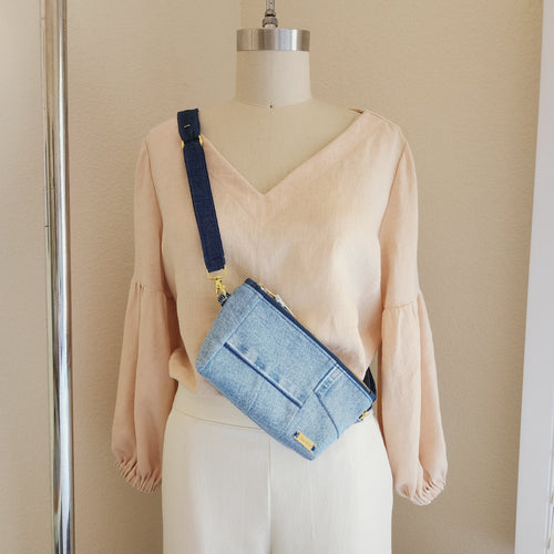 Luxurious and minimal denim crossbody / fanny bag in Denim patchwork style. The denim crossbody is hanging on mannequin across the body. Shoulder strap in dark blue denim all hardware is in gold. Luna Rose label in gold metal on bottom right. Made in Las Vegas USA
