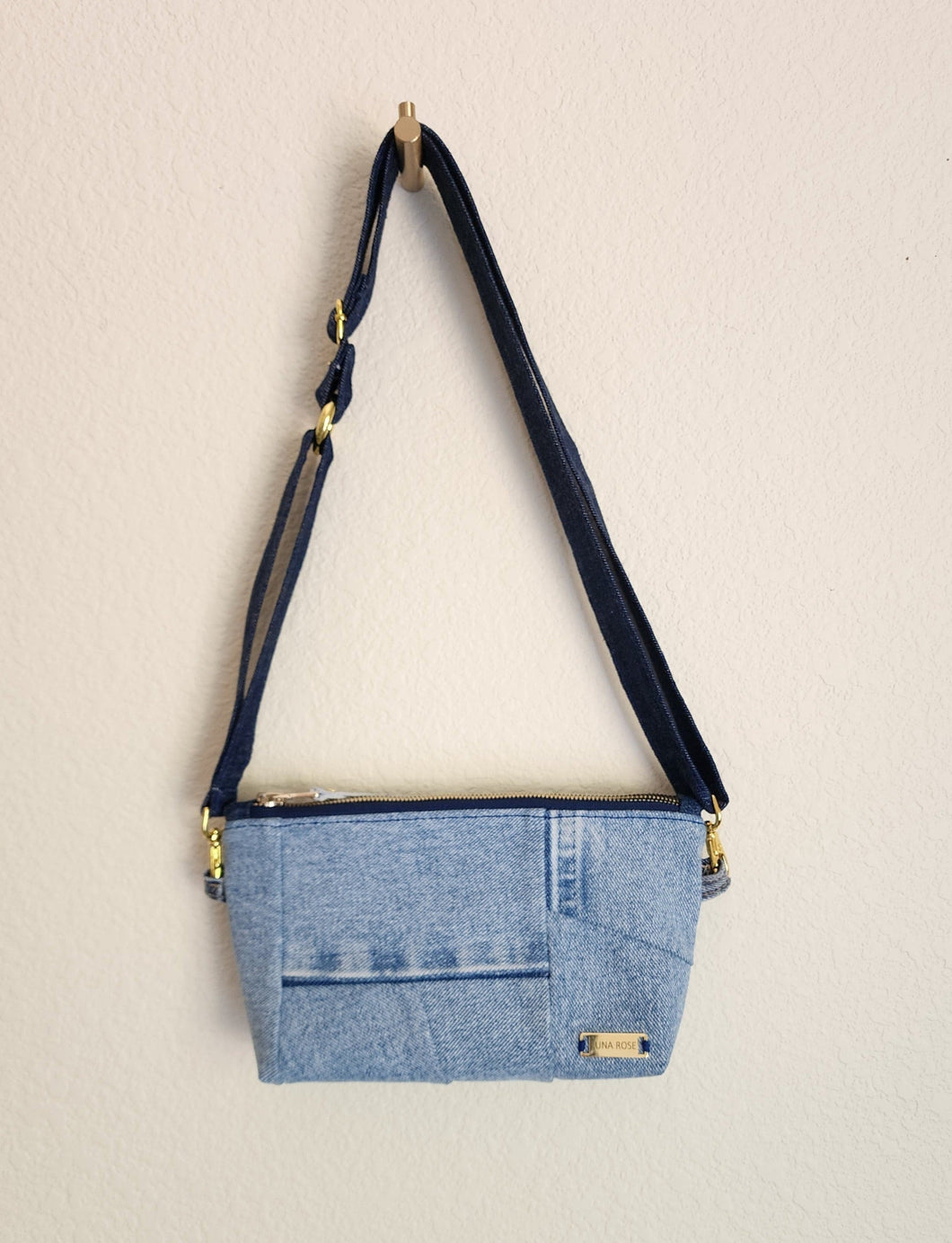 Crossbody bag showing hanging from the dark blue shoulder stap that also connects to wristlet band.  Repurposed denim to a natural luxury look. The look is soft contemporary look in repurposed denim. Great as a vegan choice.